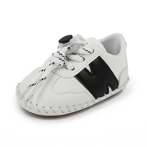 Vista lateral de zapato blanco para bebé con diseño M negro y cordones ajustables