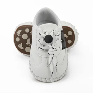 Detalle de zapatos blancos para bebé con suela de goma antideslizante y cordones.