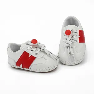 Primer plano de zapatillas blancas para bebé con logo N rojo y suelas de goma antideslizantes