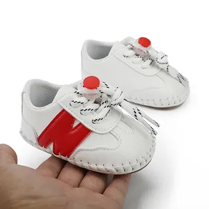 Detalle de zapatos de bebé blancos con diseño de 'N' roja y cierre de cordones