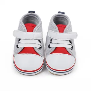 Vista frontal de zapatos de bebé grises y rojos con suela blanda y tira de velcro