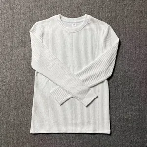 Detail view of a white men's knitted long sleeve sweater with textured waffle pattern