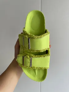 Close-up detail of neon green canvas slippers featuring fringe edges and double metal buckles