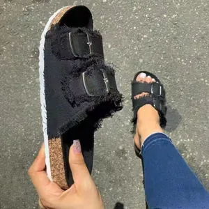 Close-up detail of black denim slides with fringe edges and double buckles