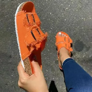 Close-up detail of orange canvas fringe slide sandals with double metal buckle straps