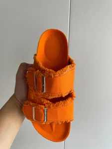 Detailed view of orange canvas slide sandals with fringe edges and metal buckles.