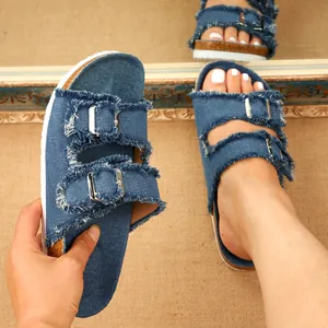 Detail shot of blue denim slippers featuring frayed edges and adjustable silver buckles.