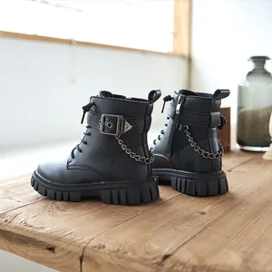Klassische schwarze Kinder-Martin-Boots mit Metallkette und Schnalle auf Holz