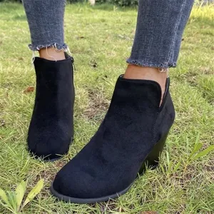 Primer plano de botines de cuña de gamuza negra para mujer sobre hierba verde.