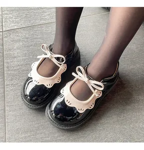 Vista detallada de zapatos de charol negro para niñas con ribete festoneado blanco y lazo