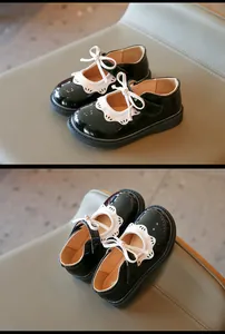 Detalle de zapatos de charol negro para niña con encaje festoneado blanco y lazo.