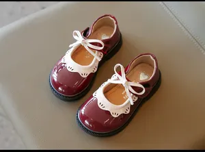 Detalle de zapatos de charol burdeos para niña con encaje blanco y lazo decorativo
