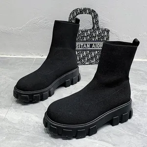 Detail of black knit sock boots with chunky platform lug soles on marble tiles.