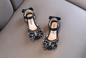 Detail view of girls' black princess shoes with rhinestone and pearl bowknot accents.