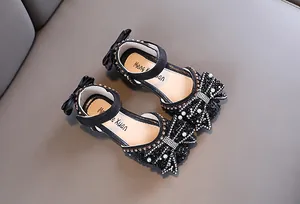 Detailed view of girls' black princess shoes with rhinestone bow and pearl accents