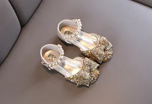 Gros plan de chaussures de princesse dorées à paillettes pour filles avec perles et nœud