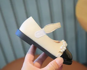 Detailansicht der cremefarbenen und schwarzen Mädchenschuhe mit eleganten Perlen.