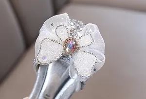Primer plano de un lazo blanco brillante con pedrería en zapatos plateados niña