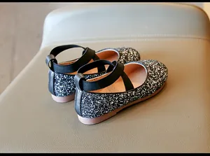 Detailed macro view of girls' glitter princess shoes featuring black cross straps and sequins.