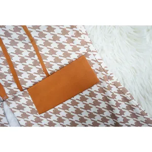Detalle de tela de traje pata de gallo marrón con bolsillo naranja sobre piel blanca.