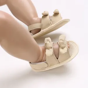 Detailweergave van beige katoenen babysandalen met strikjes op een paspopvoetje