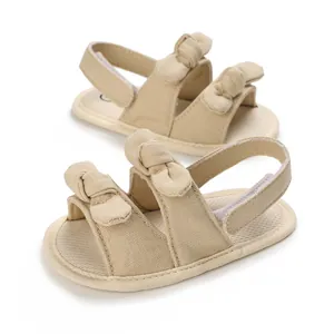 Close-up of beige baby sandals with soft cotton fabric, double bow knots and velcro straps.
