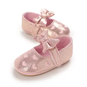 Close-up detail of pink glittery baby girl walking shoes featuring bow and heart pattern