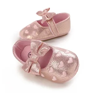 Close-up of pink glitter baby shoes with embroidered heart patterns and a bow.