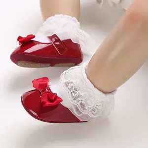 Close-up view of red patent leather baby shoes with ribbon bow and lace socks detail