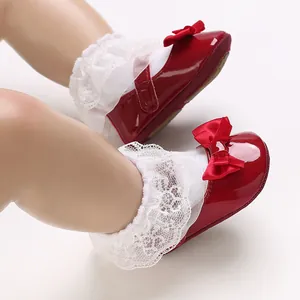Close-up of elegant red patent leather baby walking shoes featuring a decorative bow and lace socks