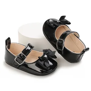 Close-up of black patent leather baby Mary Jane shoes with ribbon bows and buckles.