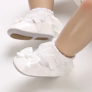Close-up detail of white infant princess walking shoes featuring lace ruffles and satin bows