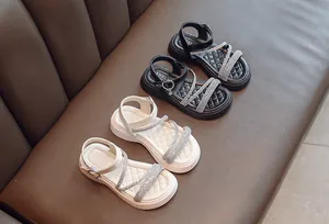 Close-up of girls' Roman sandals with rhinestone cross straps in black and white