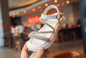 Detailed view of girls' white Roman sandals featuring sparkling rhinestone cross straps