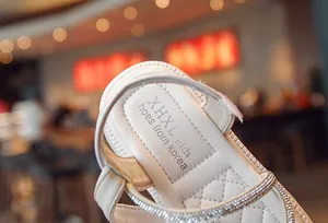 Close-up detail showing white girls leather sandals with rhinestone trim and insole logo