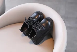 Close-up van klassieke zwarte leren schoenen voor jongens in Britse stijl op beige stoel.