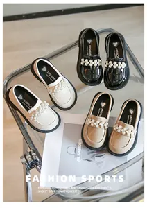 Close-up of girls' pearl loafers in black, cream, and beige on a glass table.