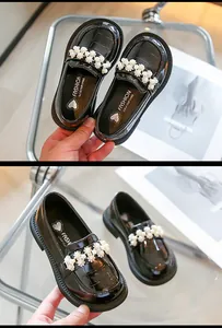 Close-up detail of black patent leather girls' loafers with elegant pearl embellishments.