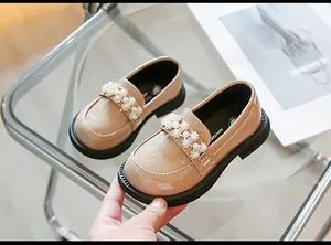 Detail view of beige girl's patent leather loafers with decorative pearl strap.