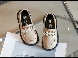 Close-up of girl's beige patent leather loafers with pearl and rhinestone floral detail.