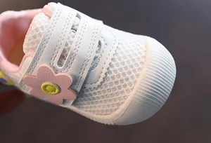 Primer plano de zapatos de malla blanca transpirable para bebé niña con flor rosa