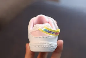 Detalle de zapato de malla blanco para bebé con talón rosa y tira trasera holográfica.