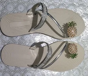Dettaglio di comodi cinturini con strass e ananas di perle su sandali piatti beige