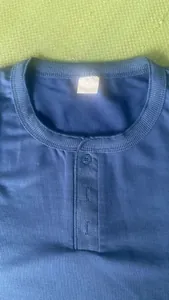 Nahaufnahme eines blauen Herren-Henley-Shirts mit XXL-Größenetikett und Knöpfen am Kragen.