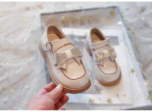 Primer plano de zapatos de charol crema para niña con lazo de diamantes brillantes.