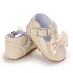 Detail view of cream baby princess shoes featuring a large bow and scalloped edges.