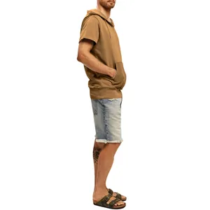 Side view of a man wearing a brown short sleeve hooded sweatshirt with denim shorts.