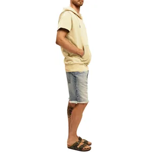 Vue de profil d'un homme portant un gilet à capuche beige sans manches et un short en jean.