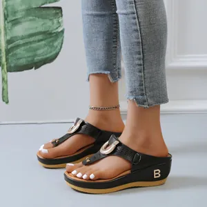 Détail élégant de tongs compensées noires montrant le logo B en métal et la lanière.