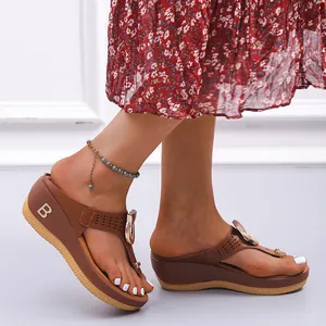 Détail de sandales compensées marron pour femme avec boucle dorée et logo B décoratif